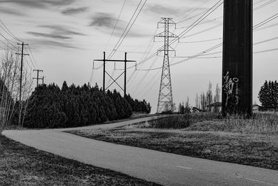 Road by electricity pylons on land against sky
