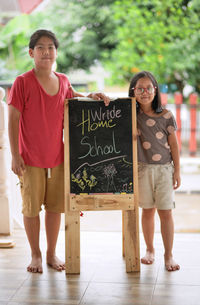 Full length portrait of sibling standing with chalkboard 