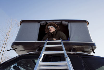 Low angle view of man sitting in roof tent on car