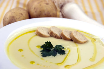 Close-up of soup served with bread in bowl by vegetables on table