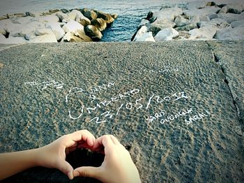 Cropped hands of woman making heart shape by text on retaining wall