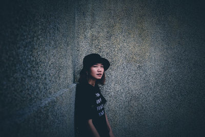 Portrait of young woman standing against wall