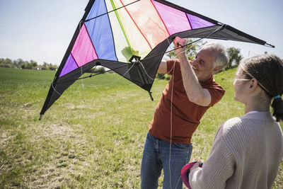 Grandfather assisting granddaughter with kite on field