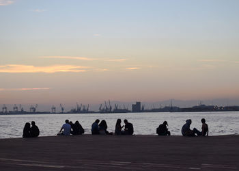 People sitting by sea against sky during sunset