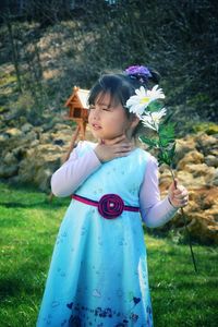 Cute girl touching her neck while holding flowers in yard