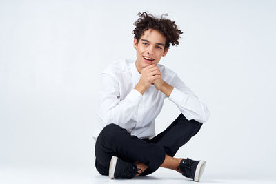 Portrait of young man sitting on seat against white background