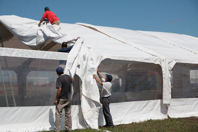 People covering greenhouse roof against clear sky