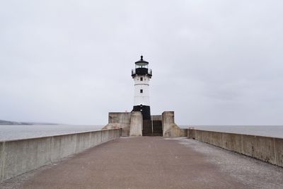 Lighthouse amidst sea and buildings against sky