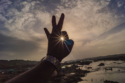 Cropped hand showing ok sign against sky during sunset