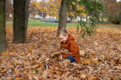 Cute boy sitting in autumn leaves in the park and laughing