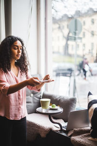 Young female influencer photographing tea and snack on table through smart phone at creative office