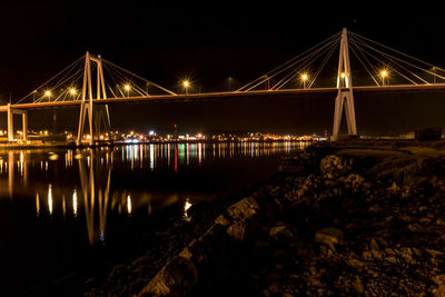 Illuminated bridge over river against sky at night