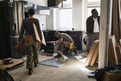 Female carpenter carrying plank while coworkers working in kitchen at site