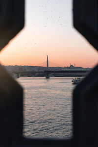 Bridge over sea during sunset seen through hole in metal