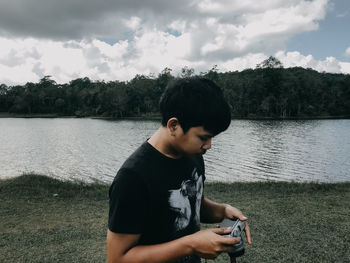 Young man looking at lake against sky