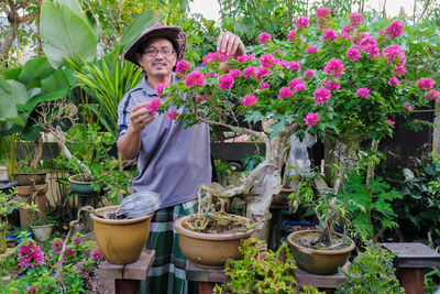 Woman holding flowers in pot standing by potted plants