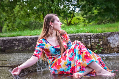 Young woman looking away while sitting by water