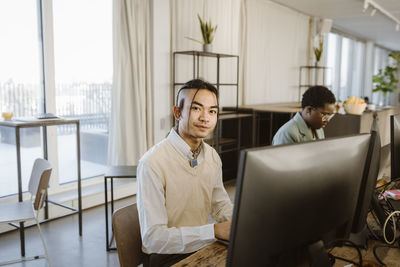 Portrait of hipster young male programmer sitting at computer desk in office