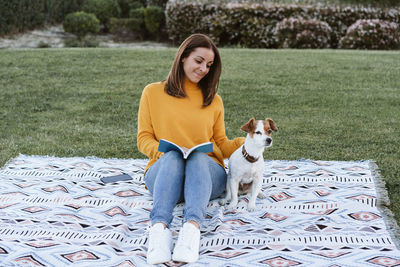 Smiling woman holding book playing with dog