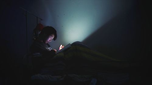 Young man reading book in darkroom at home