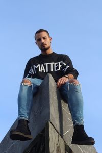 Low angle view of young man sitting against clear blue sky