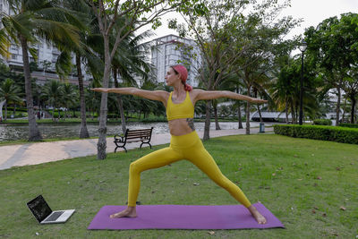 Woman with arms raised on grass against trees