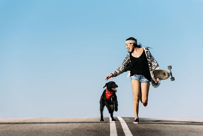 Woman with dog and skateboard against clear blue sky