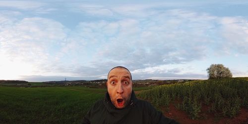 Panoramic view of man making face while standing on field against sky