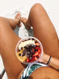 Low section of woman holding fruits at beach during sunny day