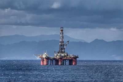 Offshore platform in sea against cloudy sky