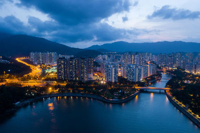 Illuminated city by river against sky at dusk