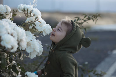 Cheerful toddler girl smelling white roses in the rose garden