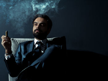 Man holding cigar while sitting on chair at night