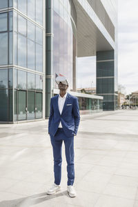 Businessman wearing virtual reality simulator standing with hands in pockets on footpath