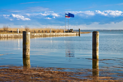 Flags on pier at lake against sky