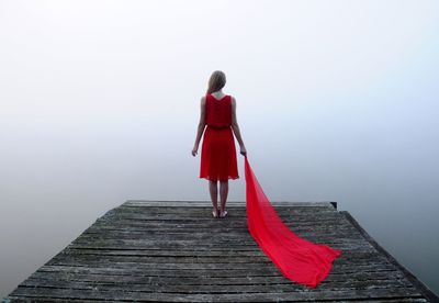 Rear view of woman standing on pier over lake during foggy weather