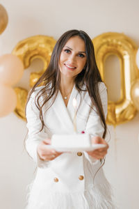 Young caucasian woman holding a birthday cake with a candle in a stylish white dress with feathers