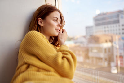 Side view of young woman looking away against window