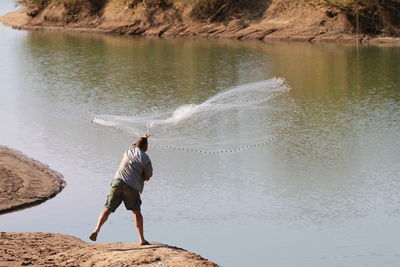 Rear view of man casting a fish net in a creek