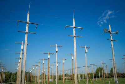 Low angle view of electricity pylons in row against blue sky
