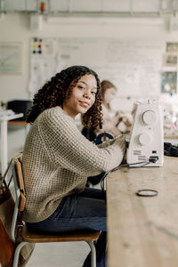 Side view portrait of female teenage student with sewing machine on desk in art class at high school