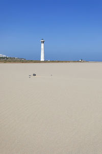 Lighthouse on beach against clear sky