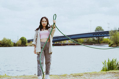 Portrait of confident young woman holding garden hose