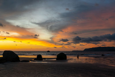 Silhouette person meditating at beach against sky during sunset