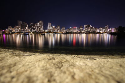 Illuminated buildings by river against sky at night