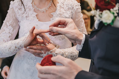 Midsection of bridegroom putting ring on bride finger