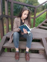 Full length of young woman using phone while sitting on bench