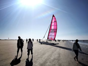 Rear view of people walking on sea shore against sky
