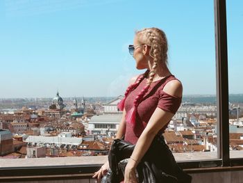 Young woman looking at cityscape against sky