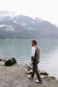 A brutal male hipster groom in a wedding suit in nature by the mountains and lake